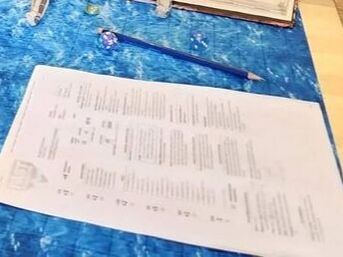 A boat sits on a water map grid with a dragon on top, two sails have fallen down onto books with the dungeons and dragons player handbook and character sheets scattered around the table. There is also a dice rolling box off to the side. 