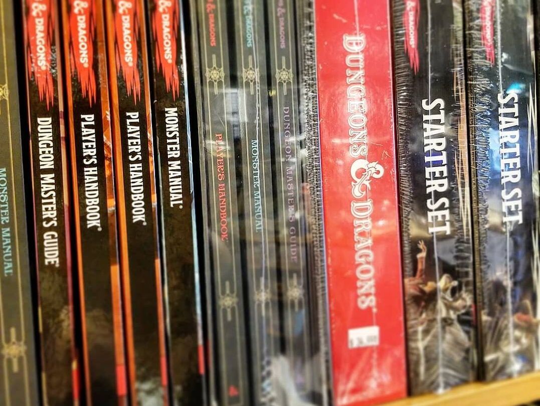 A bookshelf containing books from the famous tabletop roleplay game dungeons and dragons. There is Dungeon Master's Guide, Players Handbook, Campaign books and Starter Sets.